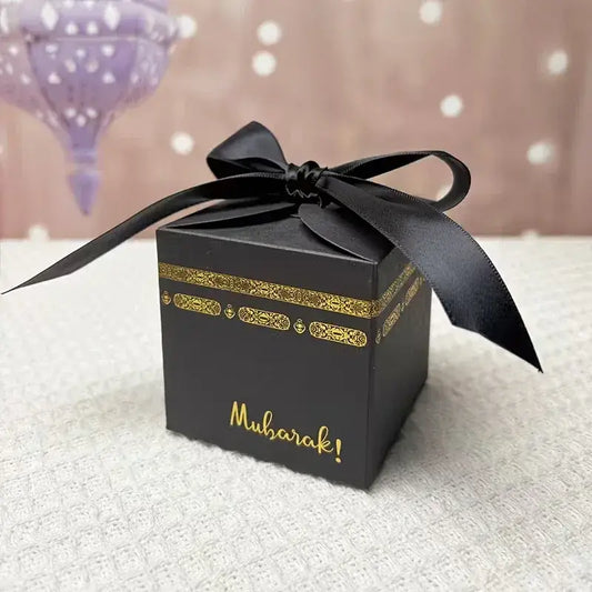 Zwarte cadeaudoosje voor hajj umrah met gouden sierlijke details en zwarte satijnen strik met muharaka tekst