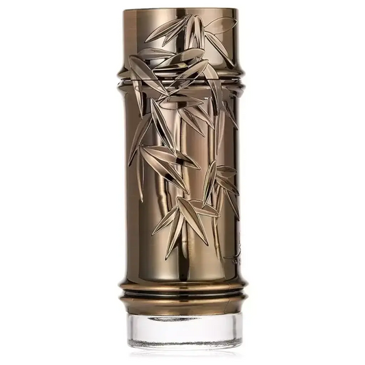 Een slanke metalen gouden parfumfles khashabi met ingewikkeld bamboebladeren reliëf en een heldere glazen basis