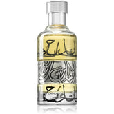 Een heldere glazen fles lattafa parfum lahdath met zilveren dop en bleke gele vloeistof versierd met arabische kalligrafie