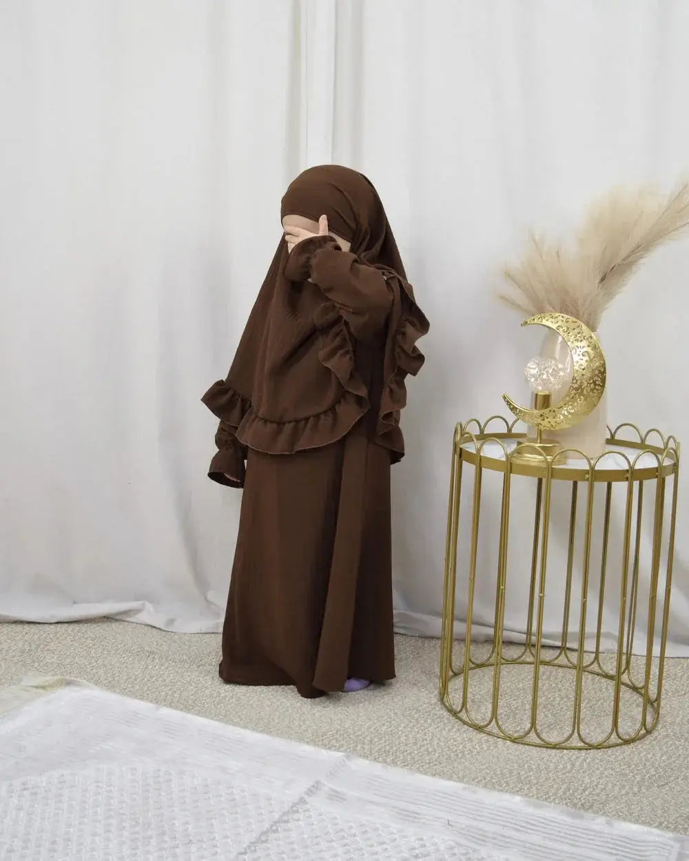 Een kind draagt een bruine abaya en bijpassende khimarset met ruffle mouwen binti stijl
