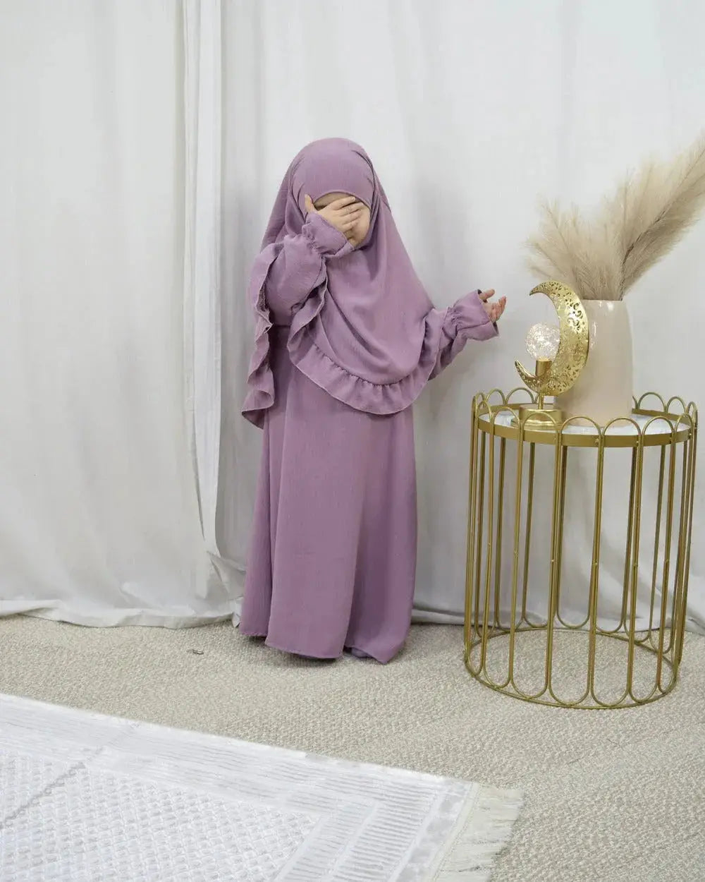 Kind draagt een lavendelkleurige abaya en bijpassende khimar met ruches uit de abaya en khimarset ruffle binti