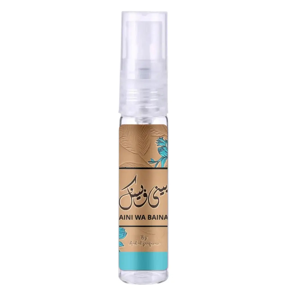 Een helder glazen sprayfles met een tan label met teal bloemen en arabische tekst van aini al perfume ard al zaafaran baini wa bainak