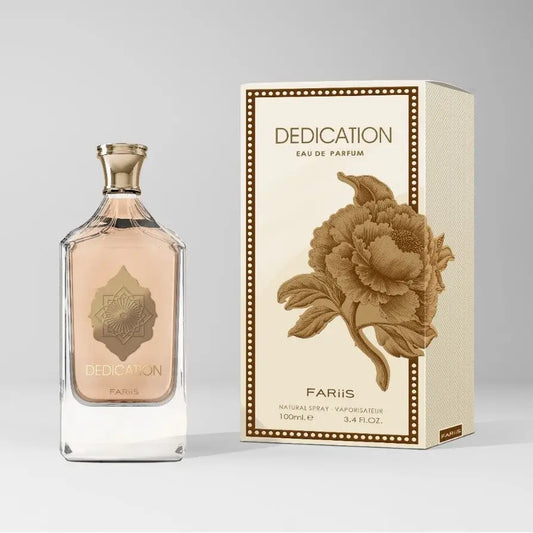 Een rechthoekige glazen parfumfles met een goudkleurige dop en reliëf gouden bloemenontwerp met lichtroze vloeistof van dedication eau de parfum door fariis