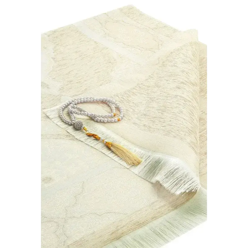Delicaat ivoorkleurig gebedskleed met subtiel patroon en franje met sierlijke kralenrosary met parelachtige kralen en gouden kwastjes uit eid cadeaupakket deen and dunya goud