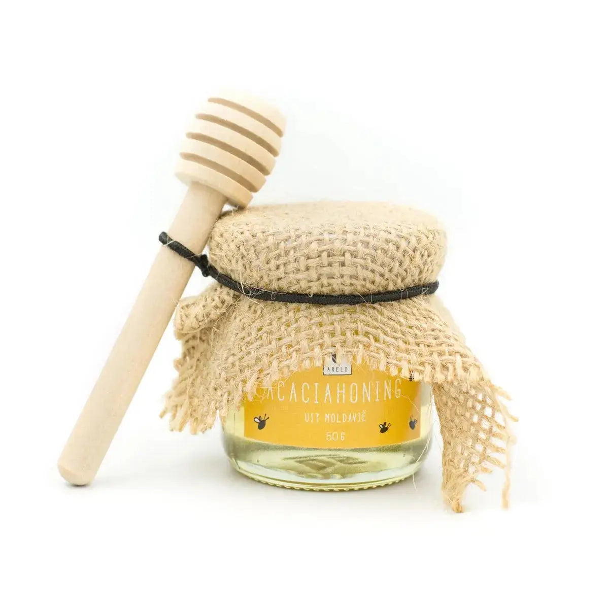 Een helder glazen pot gevuld met gouden honing, verpakt in rustiek beige jute met zwarte strik en houten dipper voor eid cadeaupakket lekker genieten luxe