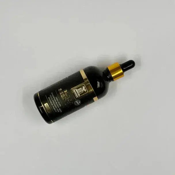 Zwarte glazen fles met gouden accenten en zwarte druppelaar van ethiopische black seed olie koud geperst 100ml