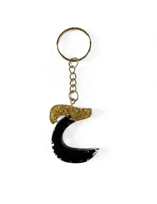 Zwarte en gouden hars sleutelhanger in de vorm van een halve maan van het merk h’aa met arabisch alfabet design