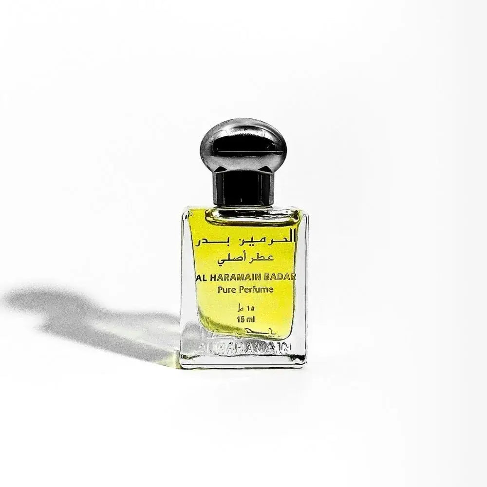 Een slanke transparante glazen fles met een zwarte bolvormige dop bevat gele al haramain badar pure parfumolie