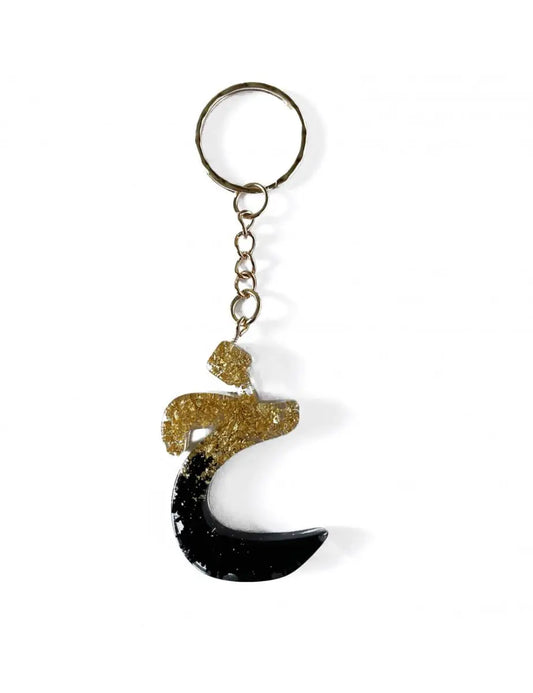 Zwarte en goudkleurige glitterige hars sleutelhanger in de vorm van de arabische letter ع met een zilveren metalen ring