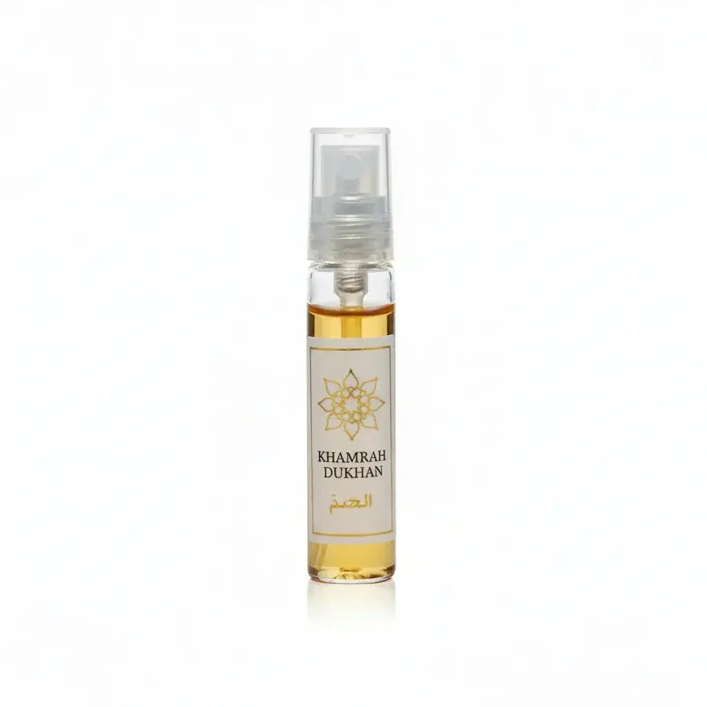 Een heldere glazen sprayfles met goudgele parfum labeled khamrah dukhan en een sierlijk gouden embleem op een wit etiket
