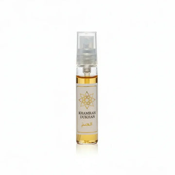 Een heldere glazen sprayfles met goudgele parfum labeled khamrah dukhan en een sierlijk gouden embleem op een wit etiket