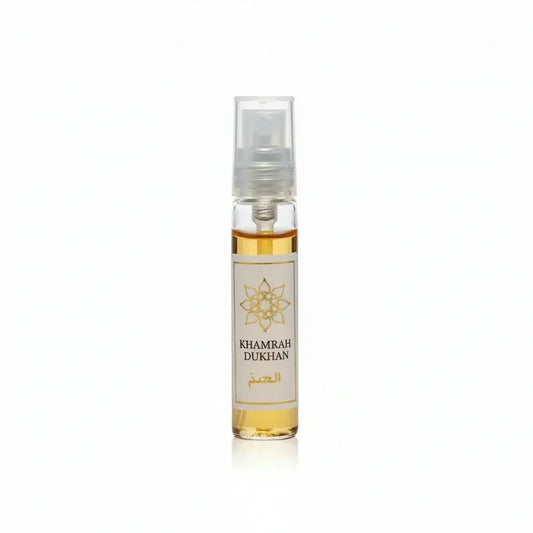 Een heldere glazen sprayfles met goudgele parfum labeled khamrah dukhan en een sierlijk gouden embleem op een wit etiket