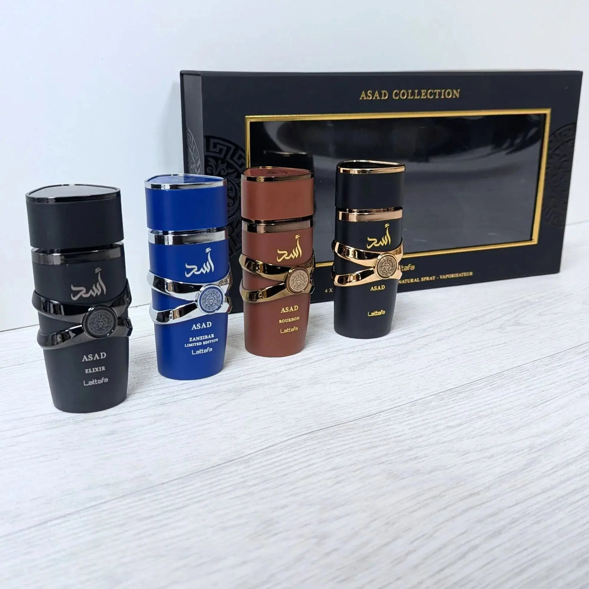 Vier slanke cilindrische parfumflessen uit de lattafa asad collectie in zwart blauw bruin en zwart met gouden accenten