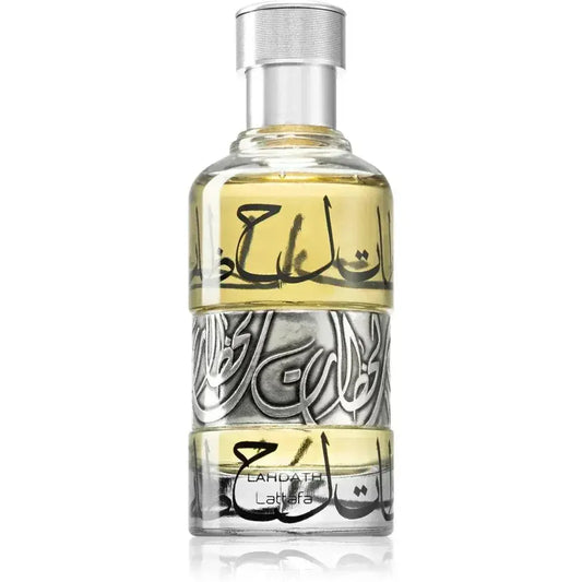 Een heldere glazen fles lattafa parfum lahdath met zilveren dop en bleke gele vloeistof versierd met arabische kalligrafie