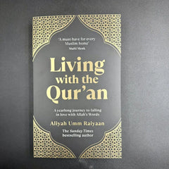Zwart hardcover boek met gouden folie en geometrische patronen, getiteld Living with the Qur’an door Aliyah Umm Raiyaan