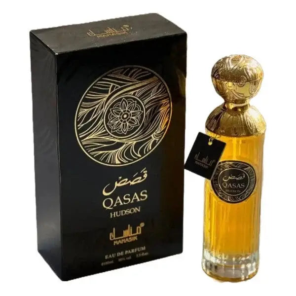 Gouden parfumfles manasik qasas hudson met ingewikkeld reliëf en bijpassende decoratieve dop naast zwarte doos met gouden arabische letters