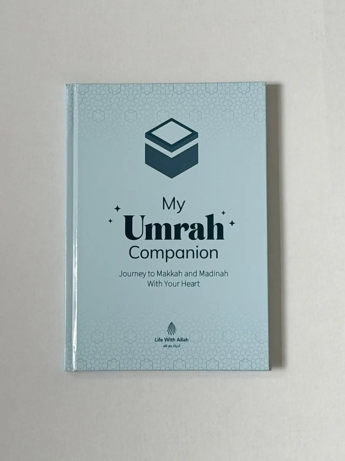 Lichtblauw hardbackboek my umrah companion met donkergroene geometrische ontwerp en subtiele rand voor umrah begeleiding