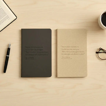 Twee minimalistische notitieboeken in donkergrijs en beige met gegraveerde nederlandse spreuken op de kaft