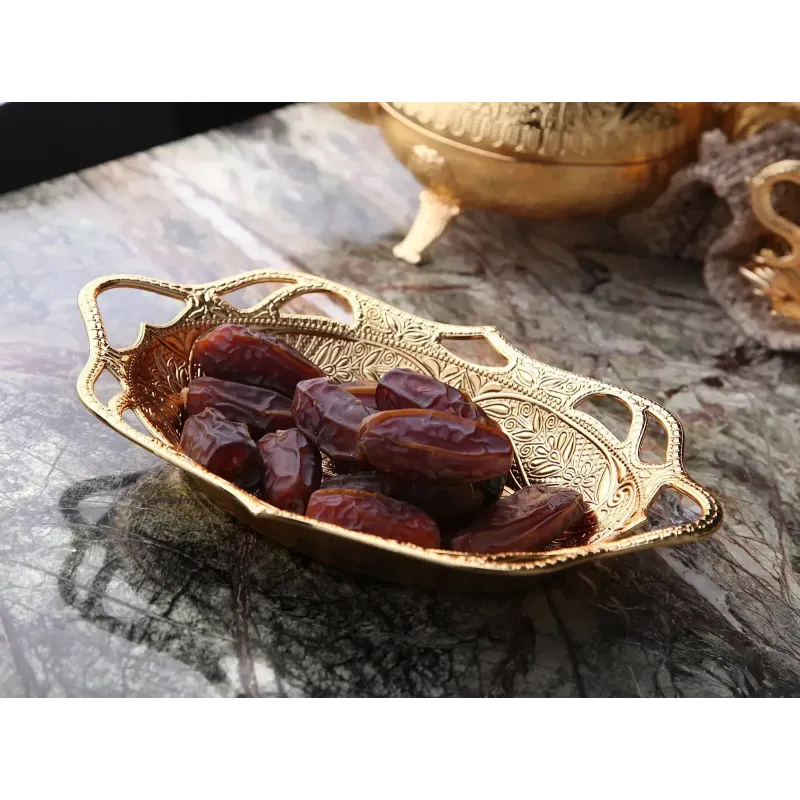 Ovale gouden sierlijke serveerschaal gevuld met donkere dadels voor dadels en snoep