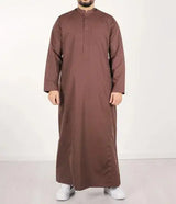 Een man draagt een lange bruine traditionele qamis ind24 met knoopsluiting en mouwen over de volledige lengte