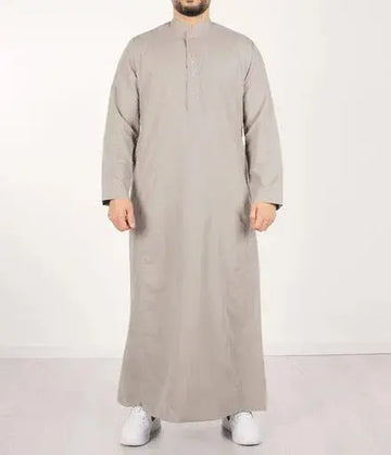 Een man draagt een lichtgrijze qamis ind24 q4him met lange mouwen, knoopsluiting en mandarijnkraag