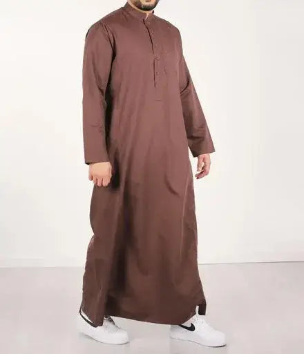 Een man draagt een lange bruine traditionele qamis ind24 met knoopsluiting en mouwen met volledige lengte