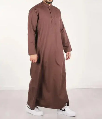 Een man draagt een lange bruine traditionele qamis ind24 met knoopsluiting en mouwen met volledige lengte
