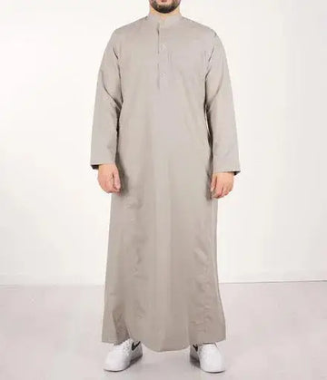 Een man draagt een lichtgrijze, floor-length qamis IND24 traditionele lange mouwen met opstaande kraag en knoopsluiting