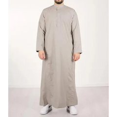 Een man draagt een lichtgrijze, floor-length qamis IND24 traditionele lange mouwen met opstaande kraag en knoopsluiting