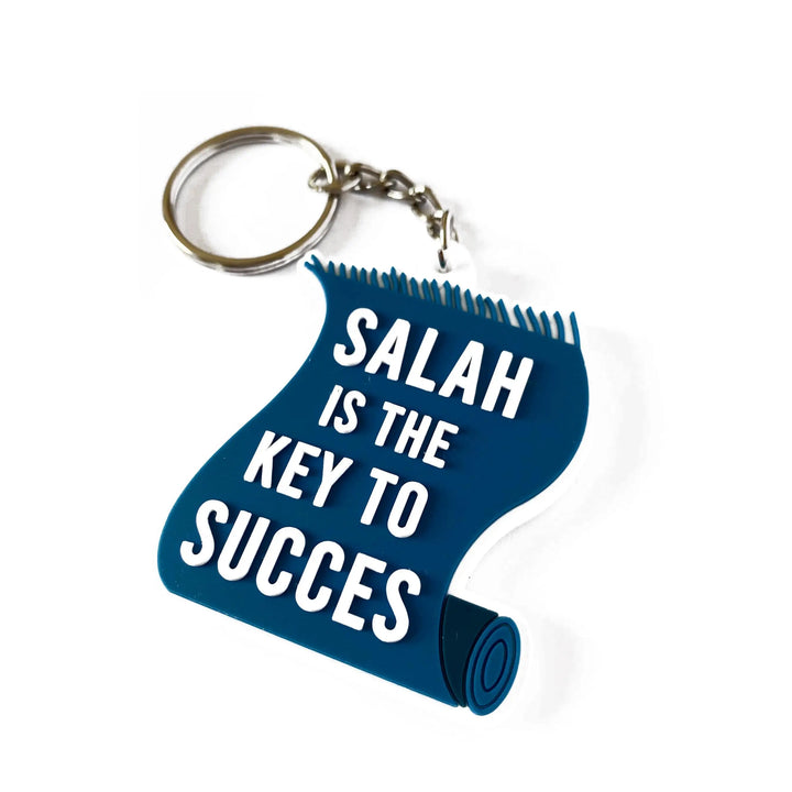 Blauwe rubberen sleutelhanger in de vorm van een opgerolde mat met witte tekst salah is de key to succes en metalen ring