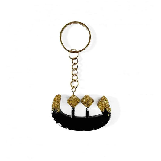 Zwarte en gouden resin sleutelhanger in de vorm van een gestileerde boot met glinsterende gouden accenten voor het arabisch alfabet