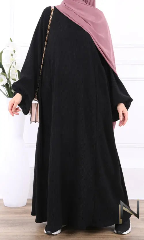 Zwart velvet papillon abaya met lange mouwen en zachte roze hijab nonchalant over één schouder gedragen