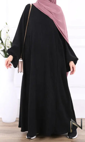 Zwart velvet papillon abaya met lange mouwen en zachte roze hijab nonchalant over één schouder gedragen
