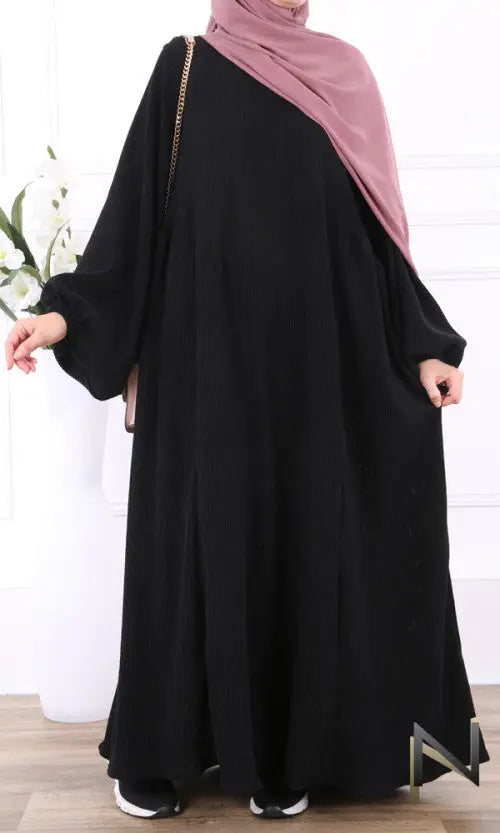 Zwarte velvet papillon abaya met roze hijab over schouder en goudkleurige kettingriem zichtbaar aan de zijkant